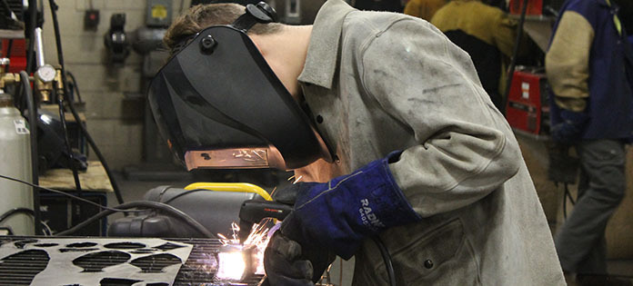 Student welding metal with mask on