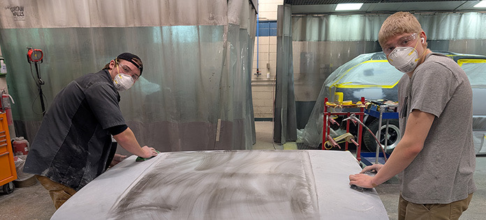 Two students sanding and prepping the hood of a car