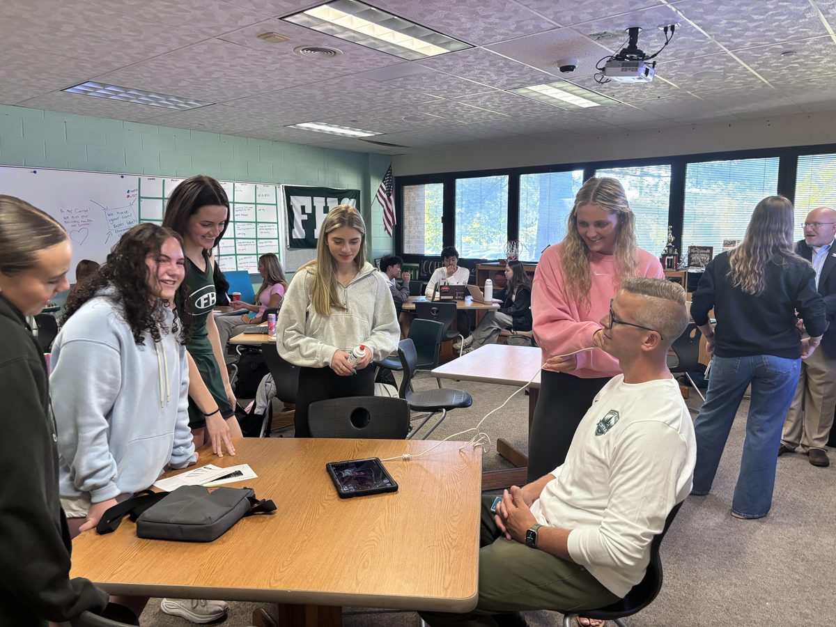 Health students gathered at a table with one hooking up a medical device to the principal