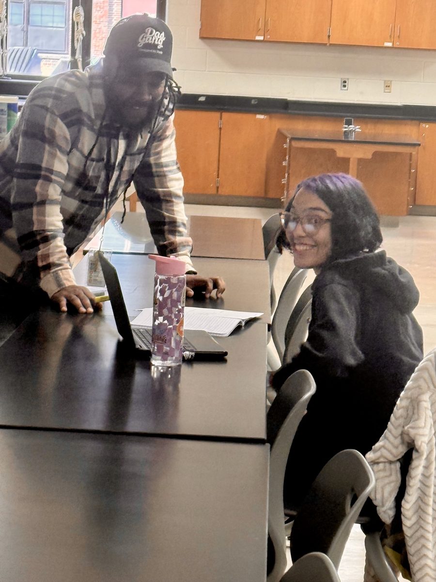 Administrator talking with a student at a table working on a laptop