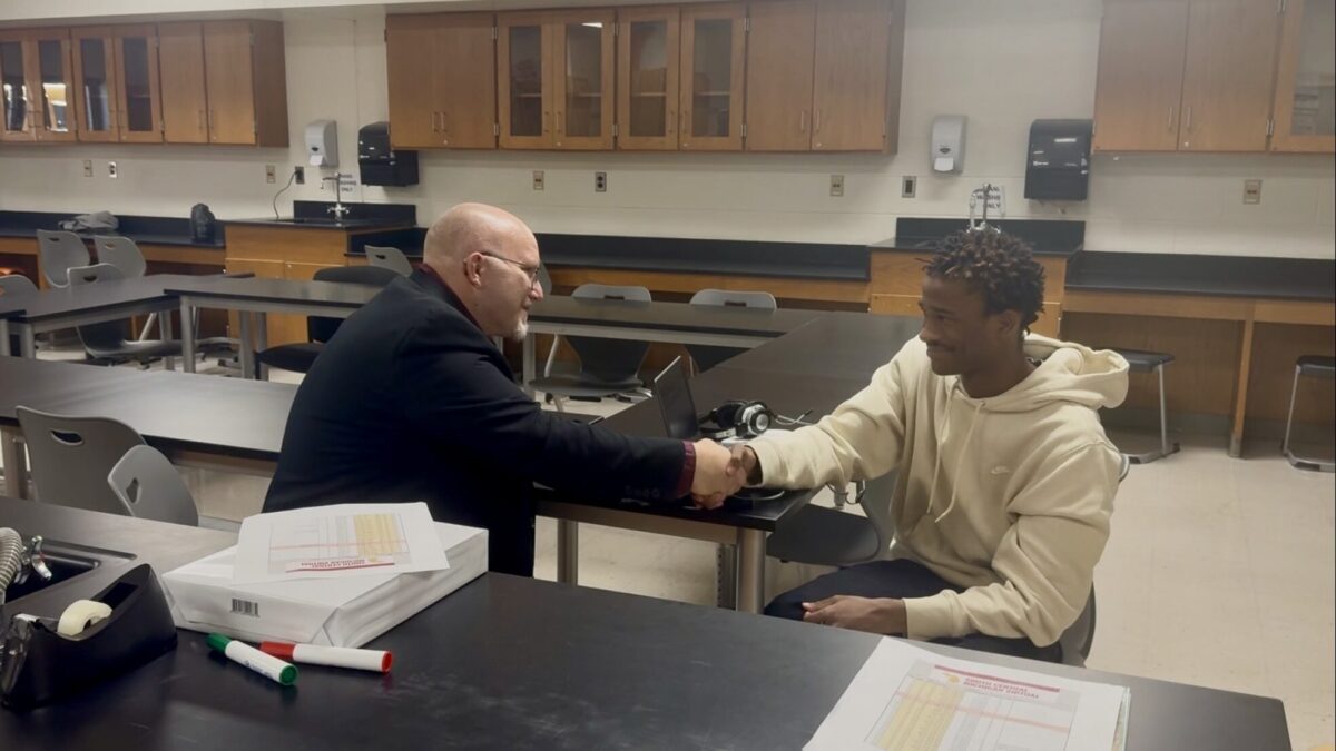 Colin shaking hands with the student while sitting at a table